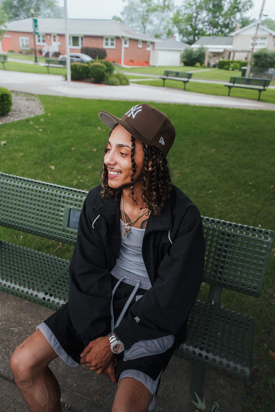 Jayggm smiling on a park bench in a brown NY fitted