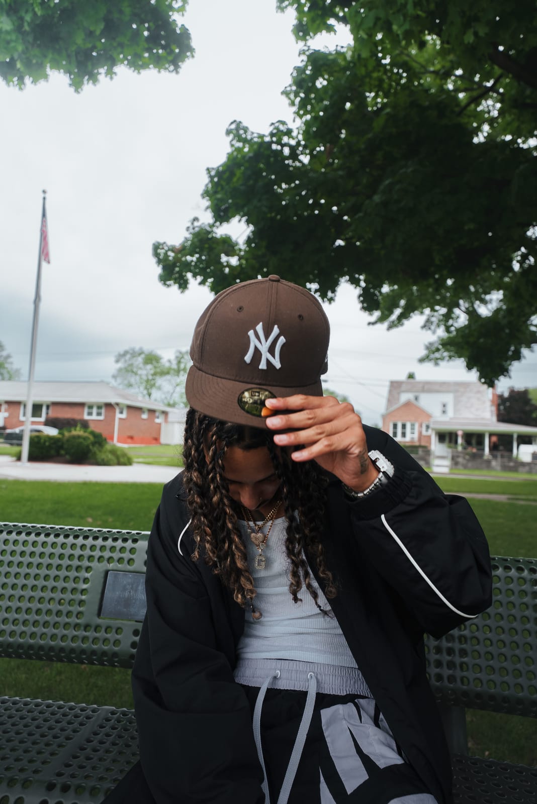 Jayggm tipping his brown NY fitted on a park bench