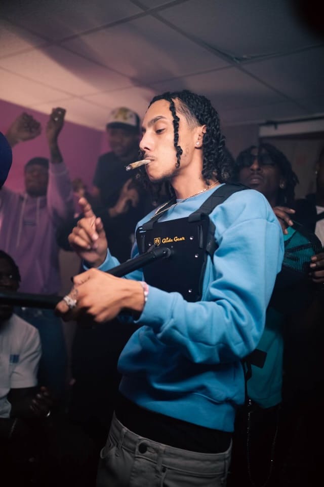 Jayggm performing with a joint and a camera rig in a blue sweater